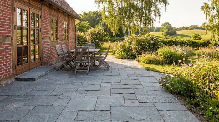 Fliseterrasse med havemøbler ved rødstenshus. Natursten og frostrisiko.