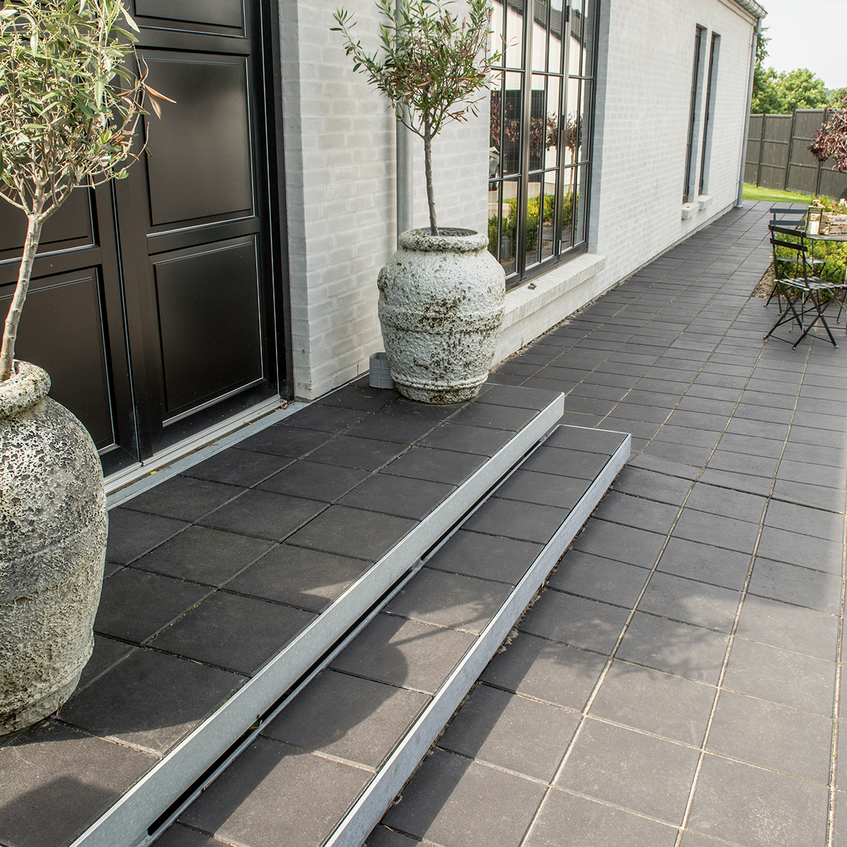 ibf sort plus fliser som terrasse ved hvidt hus med trappe og krukker.