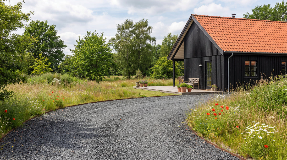 indkørsel med sort hyperit skærver (32-45 mm) ved sort træhus og vild have.