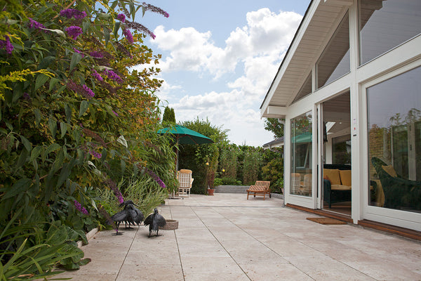 lyse travertin antik fliser på terrasse ved hus med have og fuglebad.