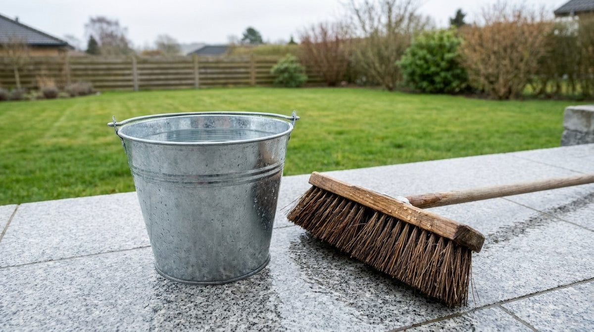 En person der skånsomt renser fliser på en dansk terrasse med kost og algerens