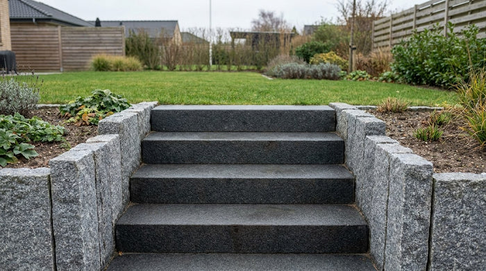 Nyanlagt udendørs havetrappe bygget med massive trappetrin i granit og indrammet af lodrette granitkantsten som vanger mod havebedet.