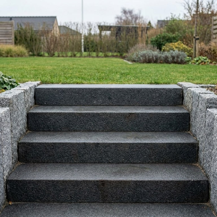 Nyanlagt udendørs havetrappe bygget med massive trappetrin i granit og indrammet af lodrette granitkantsten som vanger mod havebedet.