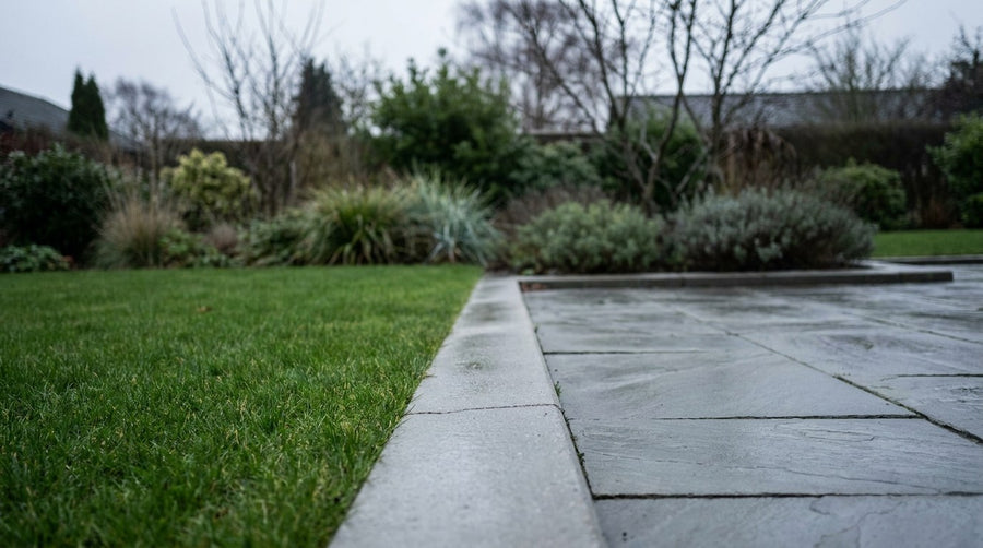 En nylagt række af kantsten beton sat i jordfugtig beton langs kanten af en indkørsel