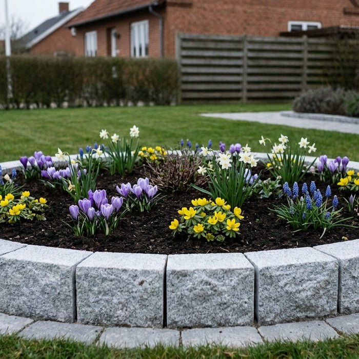 Et færdigbygget rundt højbed i lys grå portugisisk granit med frodige grønne planter i en dansk have