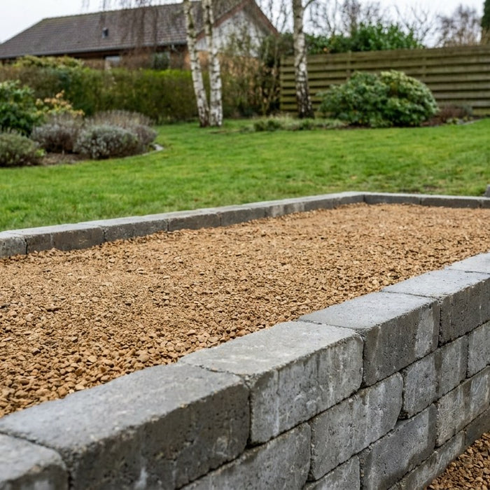 En nyanlagt hævet terrasse opbygget med solide grå støttemurblokke i beton og store naturstensfliser på toppen, omgivet af en velplejet dansk have.