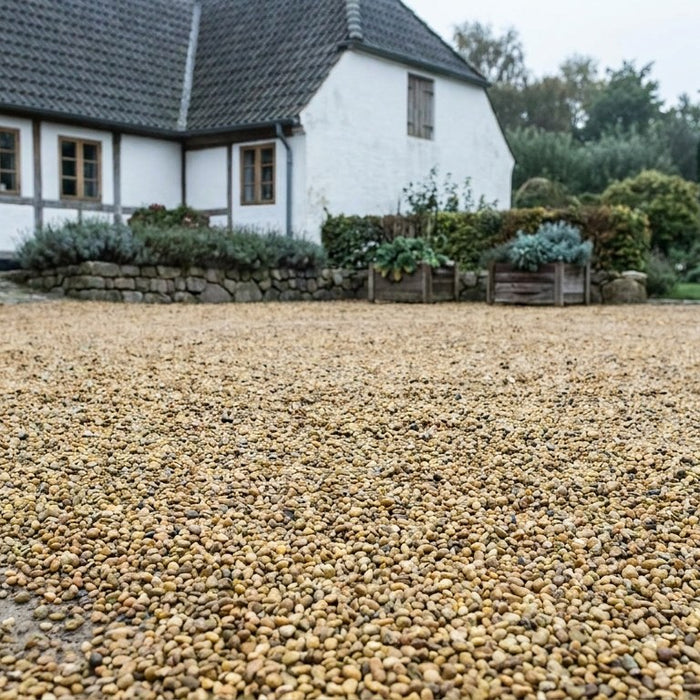 En idyllisk landlig gårdsplads belagt med flotte grå ærtesten, hvor en bil er parkeret uden at grave sig ned i underlaget.