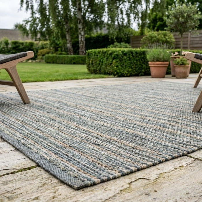 Lækkert loungemiljø på en terrasse med keramiske fliser, hvor et gråt udetæppe samler møblerne og beskytter belægningen.