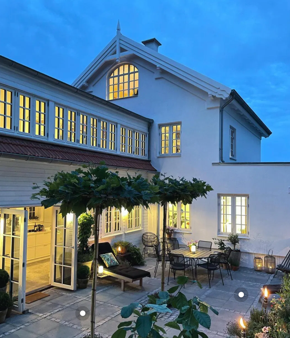 Fliser med chaussesten på en hyggelig terrasse ved et hvidt hus i skumringen.