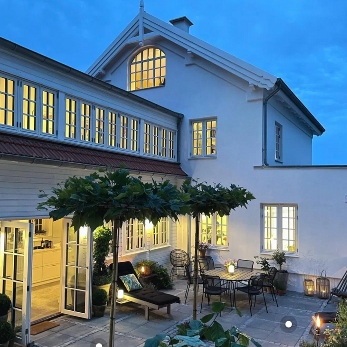 Fliser med chaussesten på en hyggelig terrasse ved et hvidt hus i skumringen.