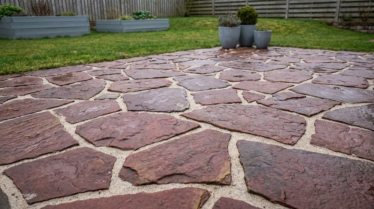 En smuk og færdiganlagt terrasse belagt med nexøbrud i varme røde og gyldne nuancer, omkranset af frodige haveplanter.