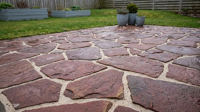 En smuk og færdiganlagt terrasse belagt med nexøbrud i varme røde og gyldne nuancer, omkranset af frodige haveplanter.
