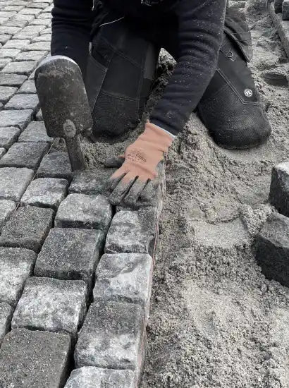 Anlægsgartner lægger brosten til indkørsel. Sand og brosten ses.