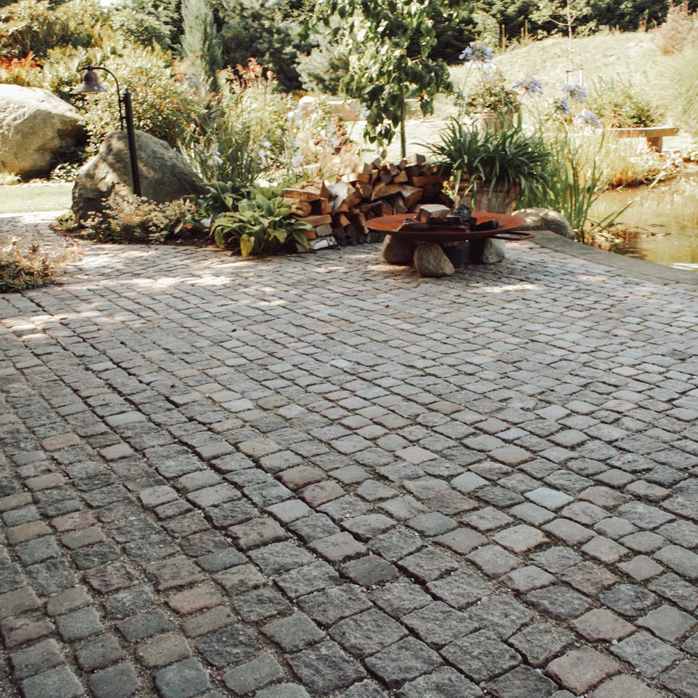 Chaussestenbelægning i have med bålplads og dam.