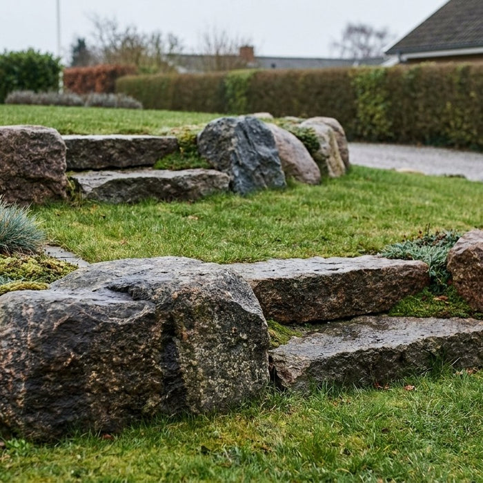 Stor kampesten brugt som naturlig dekoration og støttemur i et skrånende dansk havedesign