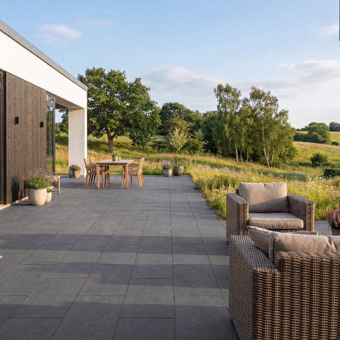 Terrasse med keramiske fliser, havemøbler og udsigt over grønne marker.