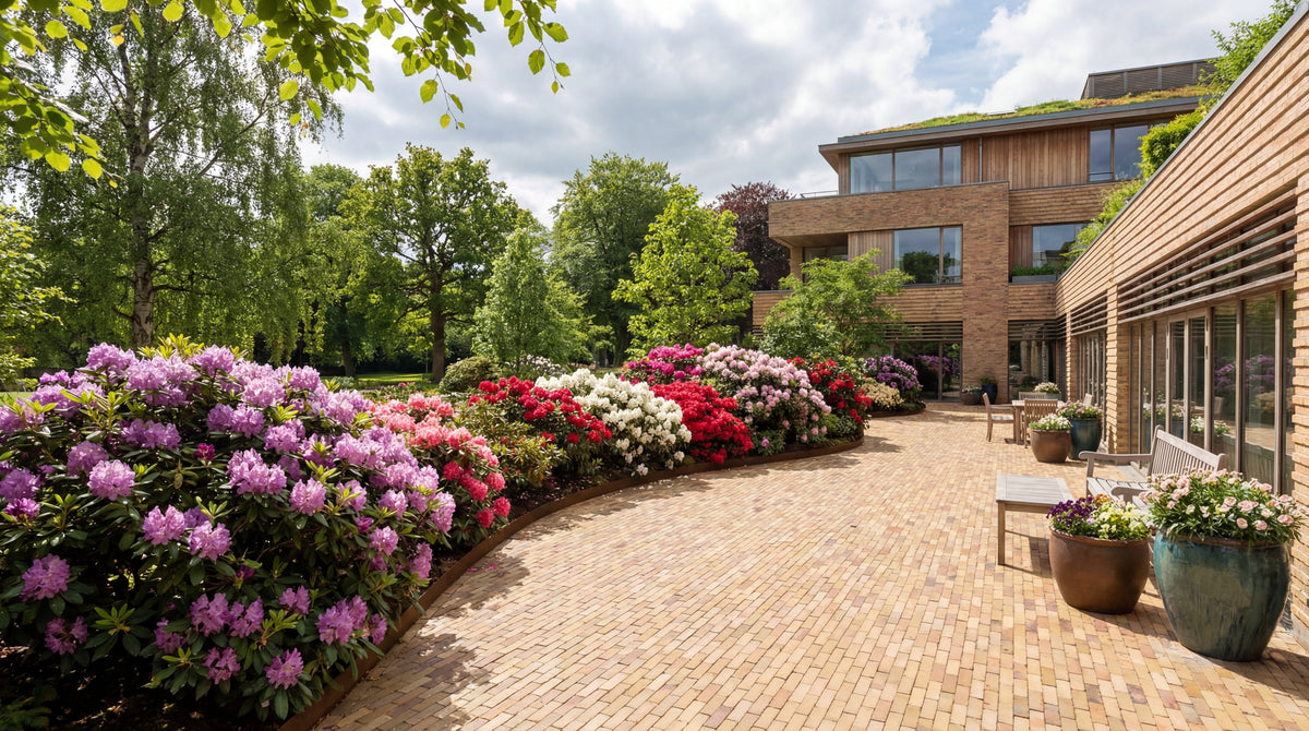 Terrasse med teglklinker, blomsterbed og moderne hus.