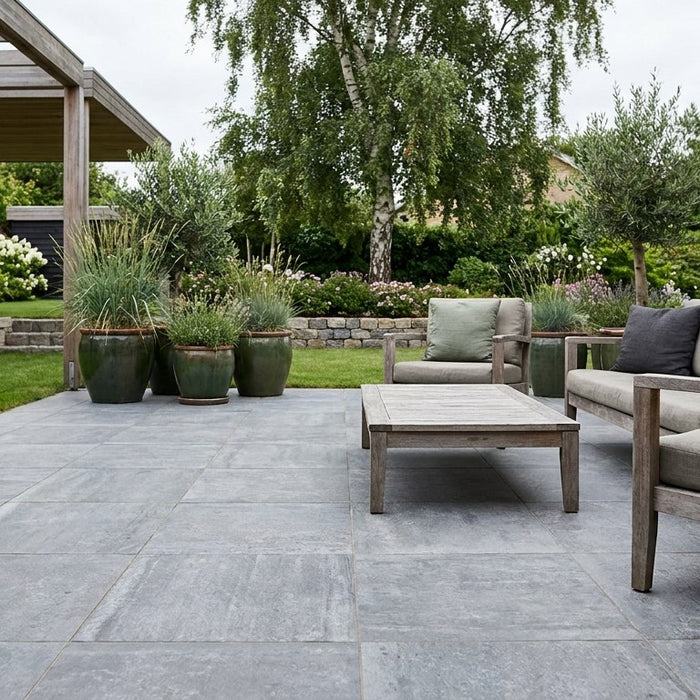 Smuk udendørs terrasse anlagt med en kombination af keramiske fliser i storformat og kantning af brosten.