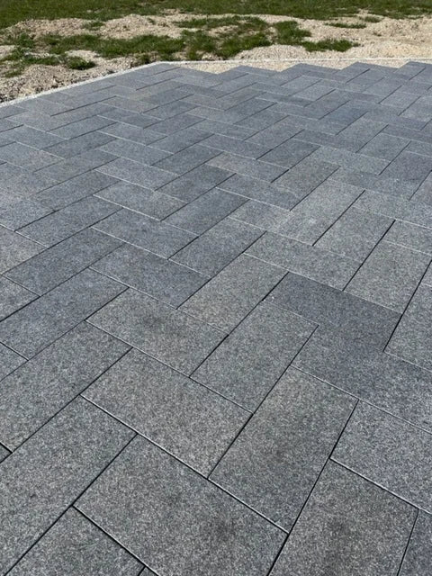 Grå granitfliser lagt i sildebensmønster på en terrasse.
