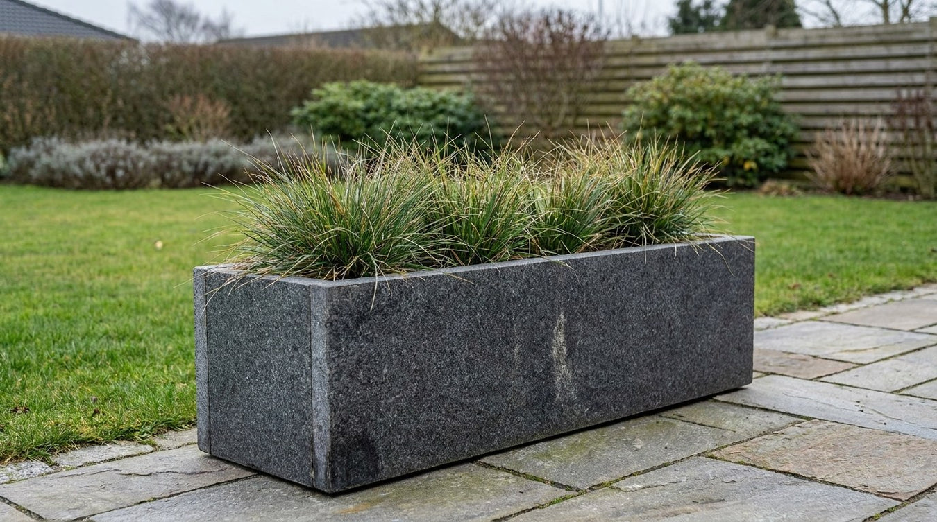 Plantekumme i mørk granit beplantet med græs på terrasse