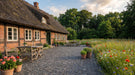 terrasse med sorte halve chaussesten ved bindingsværkshus og blomstereng.